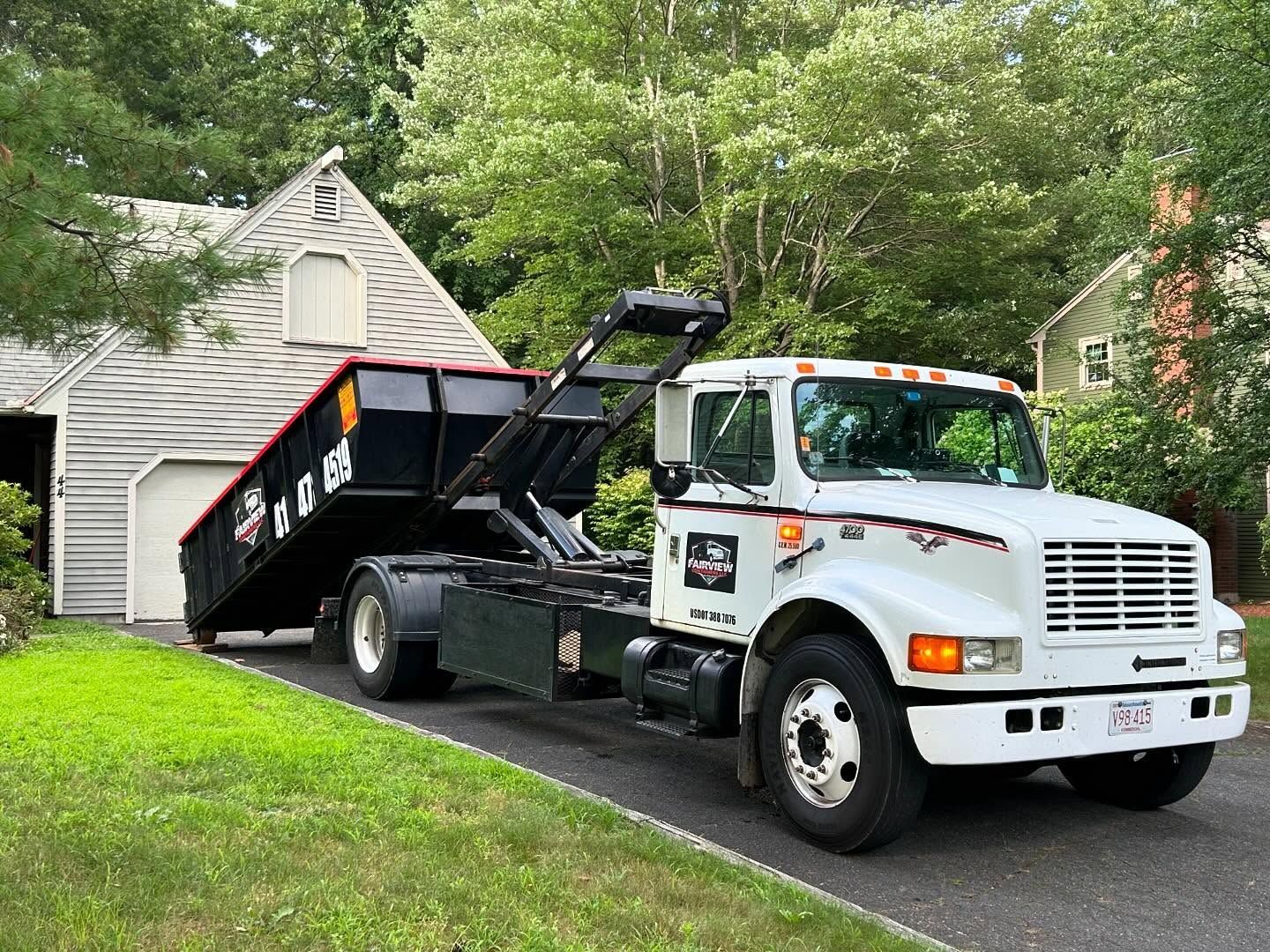 White dump truck with a black container on a residential driveway.