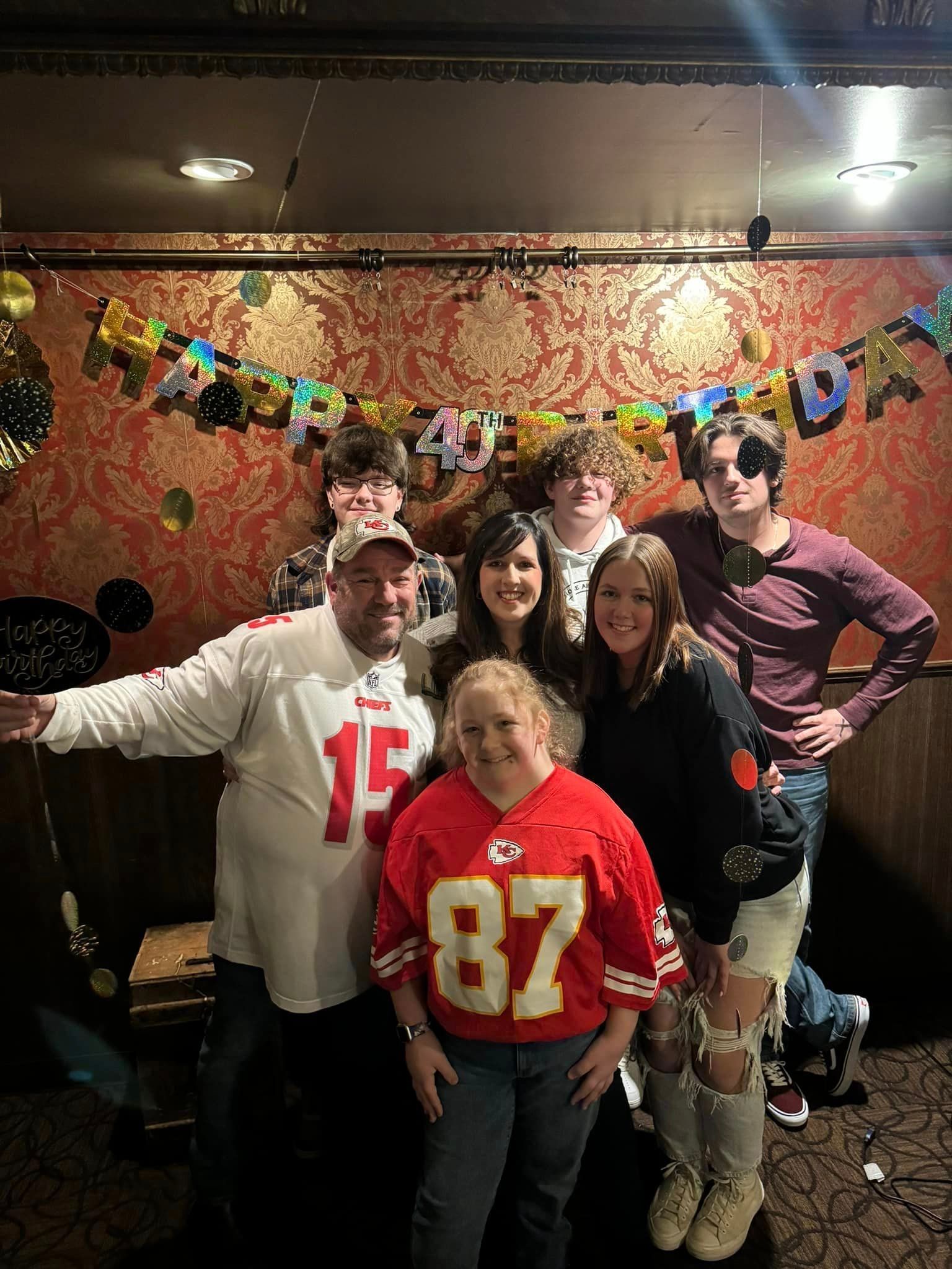 A group of people are posing for a picture in a room with balloons on the wall.