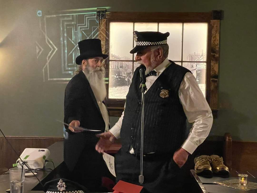 Two men in top hats are standing in front of a microphone.