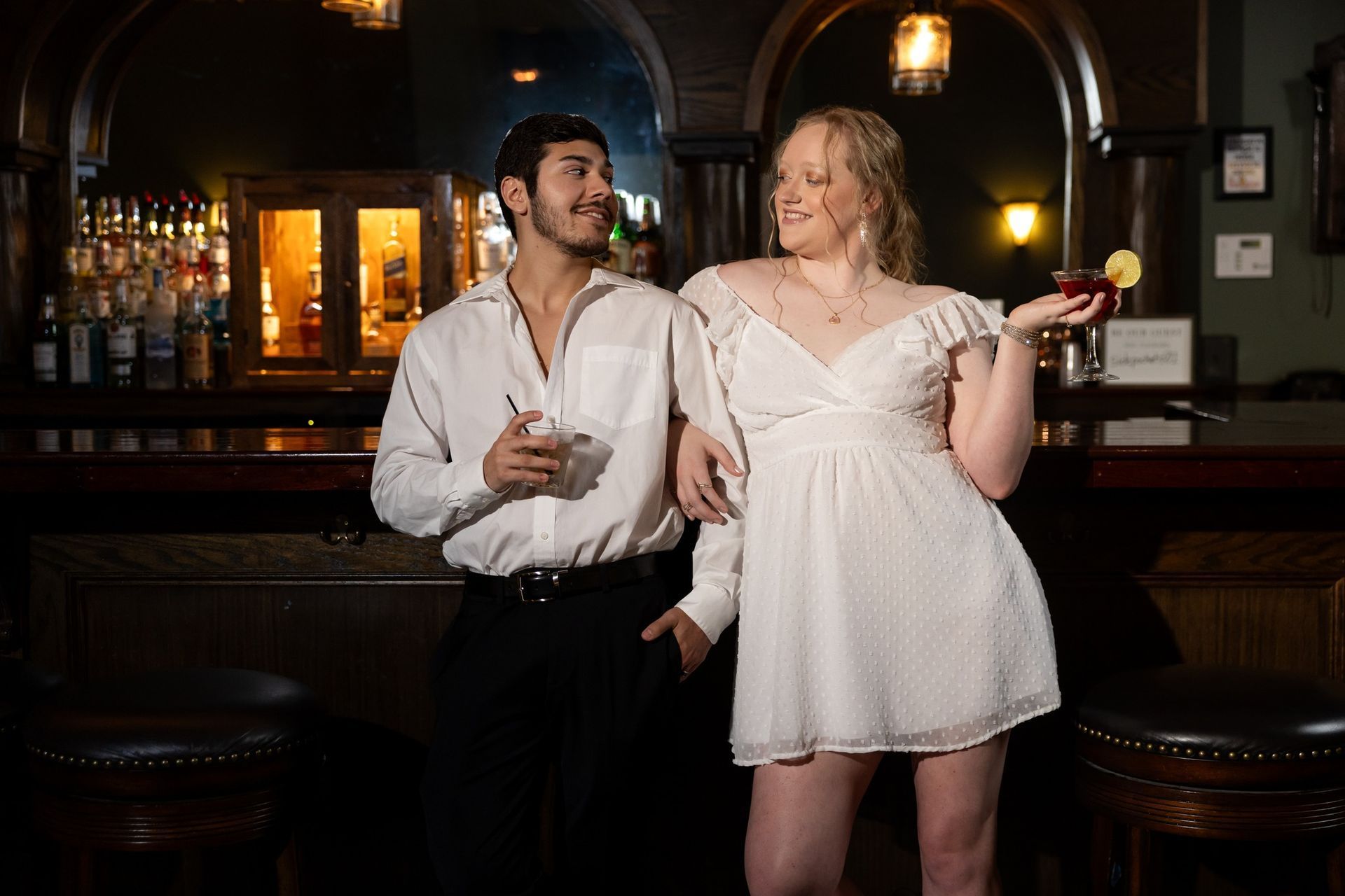 A man and a woman are standing at a bar holding drinks.