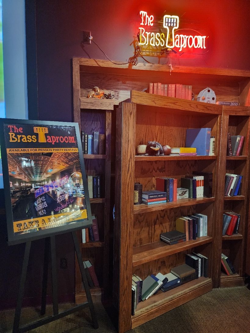 A bookshelf with a sign that says the brass taproom on it.