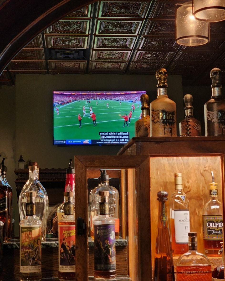 A bar filled with bottles of liquor and a television with a football game on it