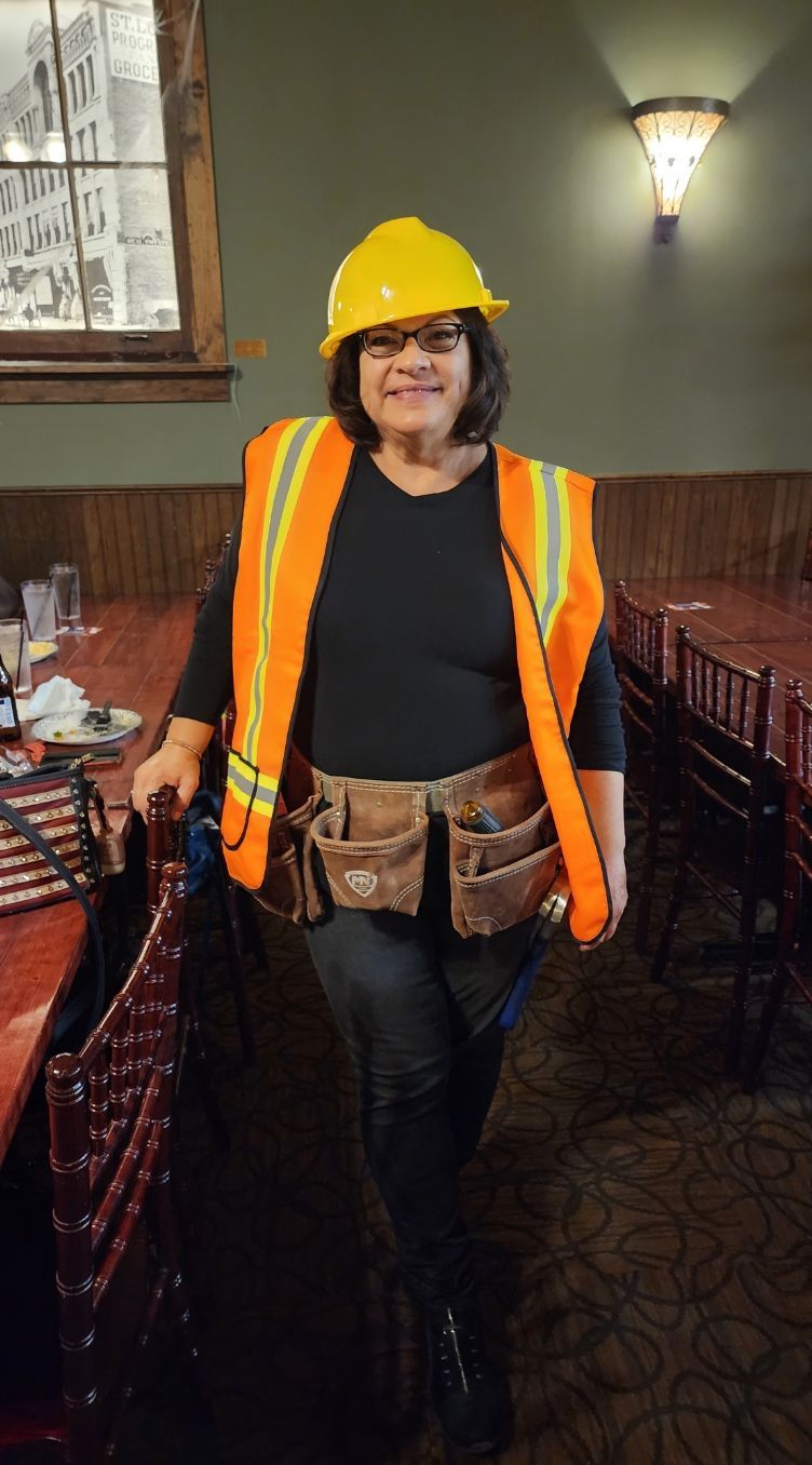 A woman wearing a hard hat and safety vest is standing in a restaurant.