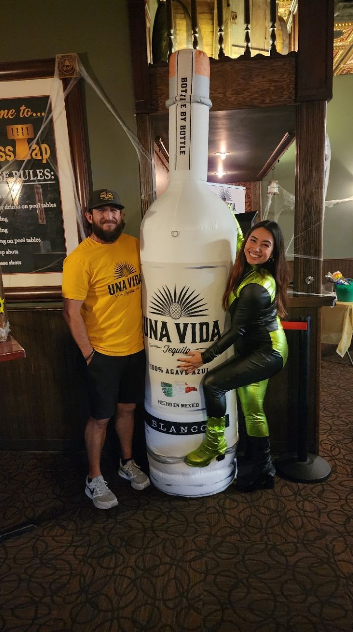 A man and a woman are standing next to a giant bottle of tequila.