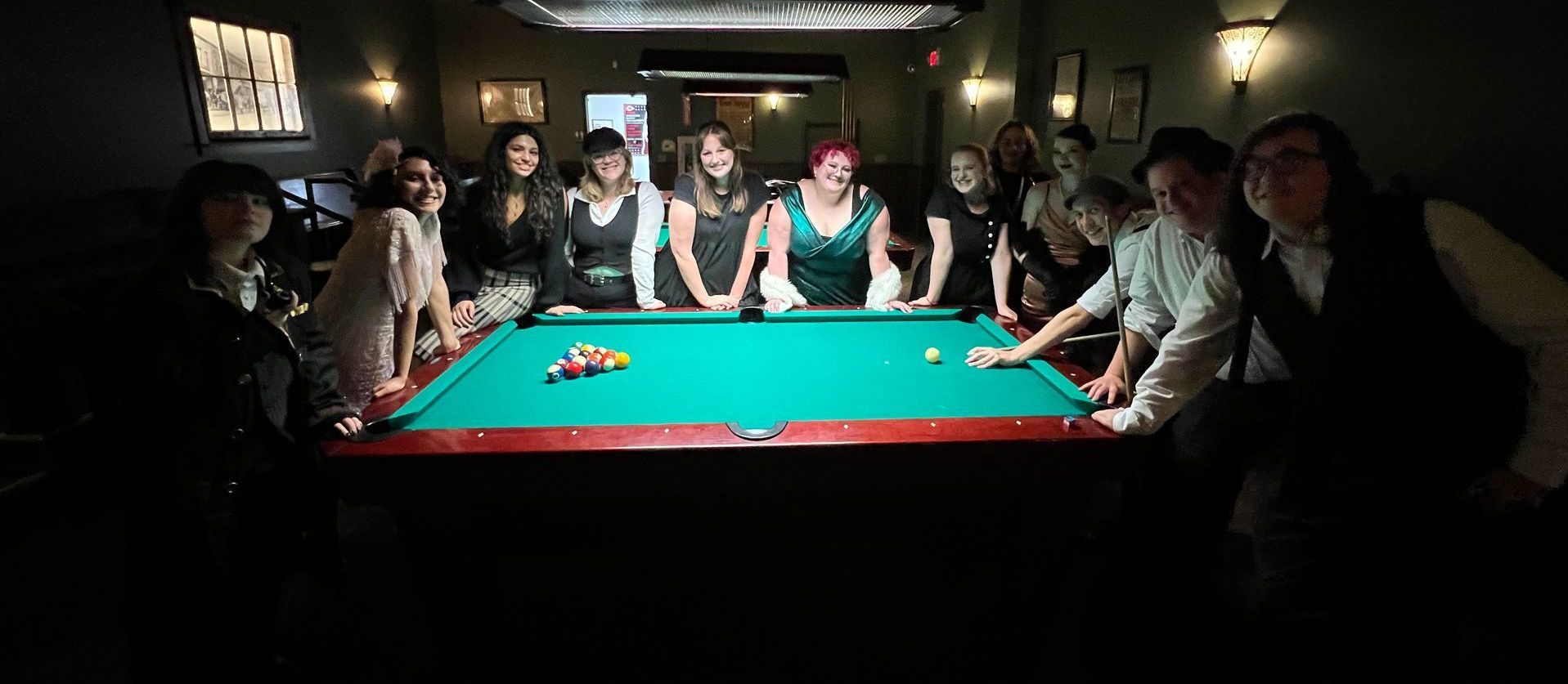 A group of people are standing around a pool table