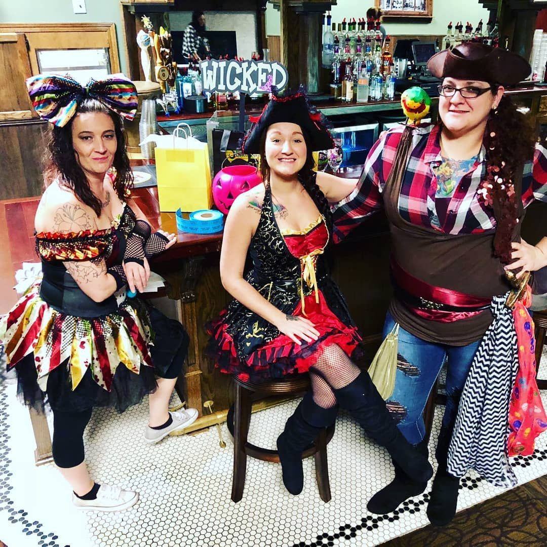 Three women in halloween costumes are posing for a picture in front of a sign that says wicked