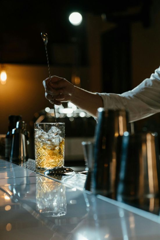 A bartender is mixing a drink with a spoon in a glass.