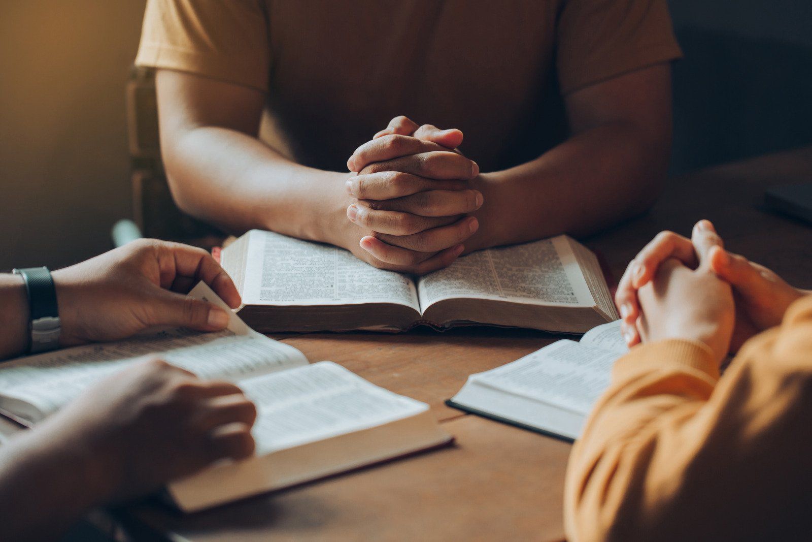 A group of people are sitting at a table with their hands folded in prayer.