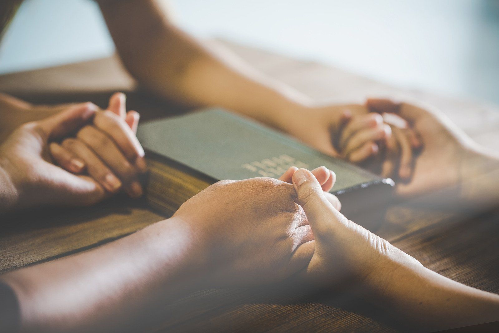 A couple of people are holding hands over a bible.