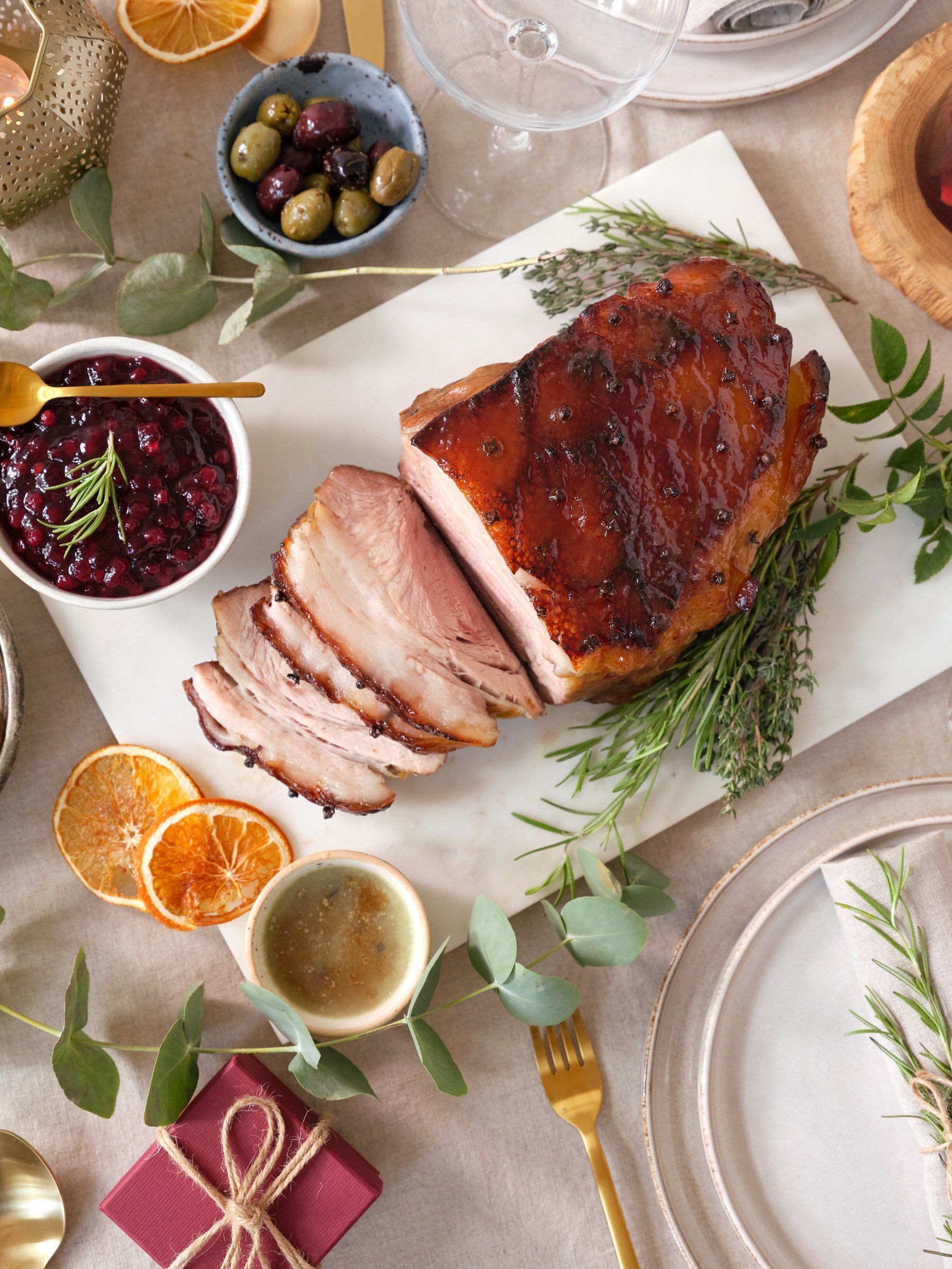 A ham is sitting on a white cutting board on a table.