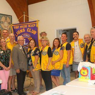 A group of people are posing for a picture in front of a lions club banner.