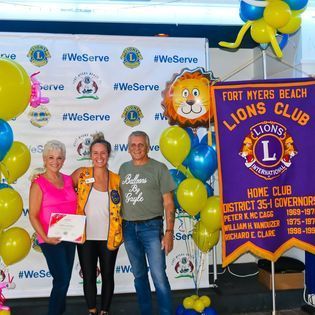 A group of people standing in front of a lion 's club banner and balloons.