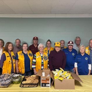 A group of people are posing for a picture in front of a table filled with food.