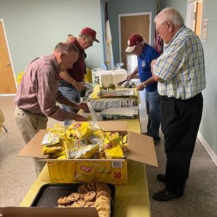 A group of men are standing around a table with boxes of food.