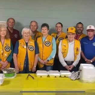 A group of people wearing yellow vests are standing around a table.
