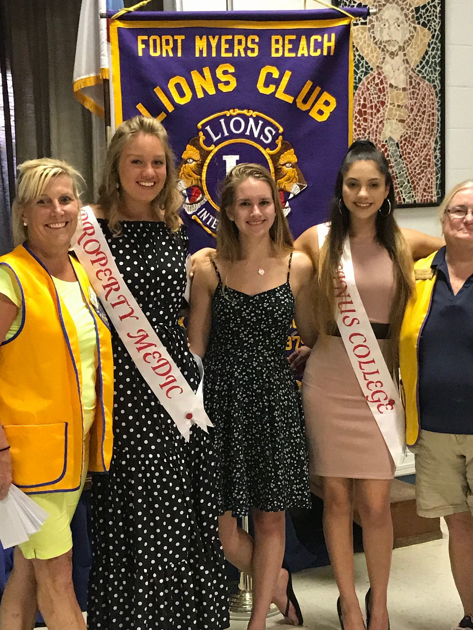 A group of women standing in front of a fort myers beach lions club banner