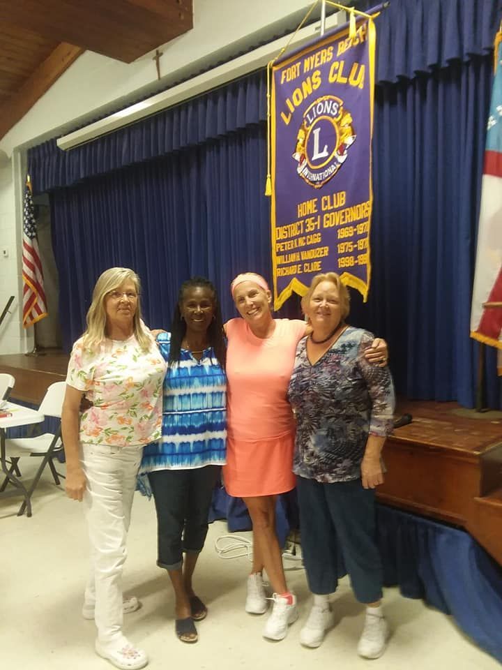 Four women are posing for a picture in front of a banner that says lions club