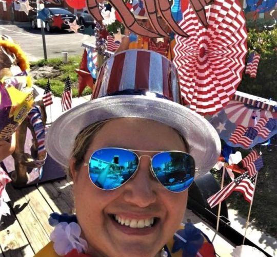 A woman wearing a patriotic hat and sunglasses is smiling