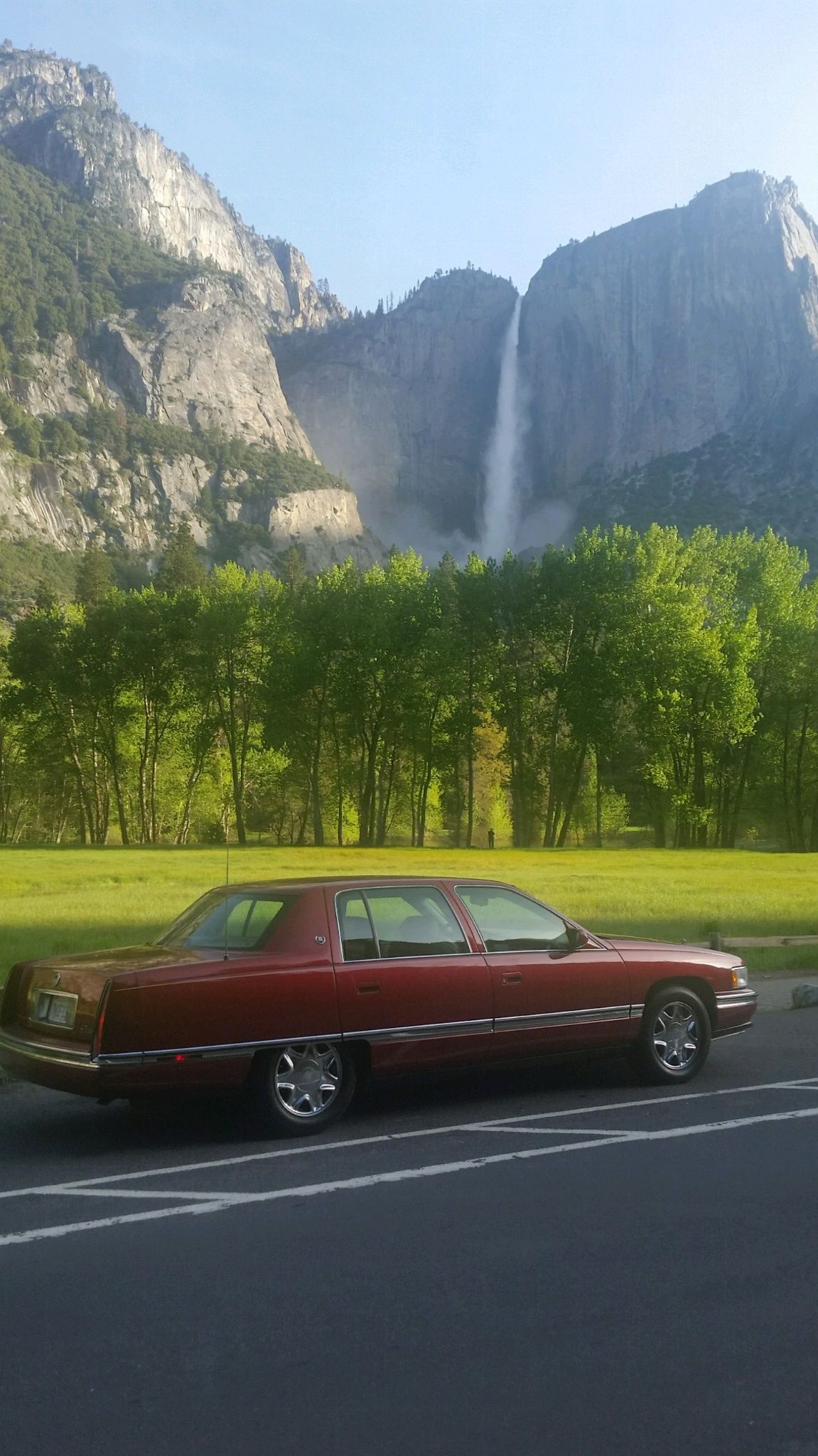 A red car is parked in front of a waterfall.