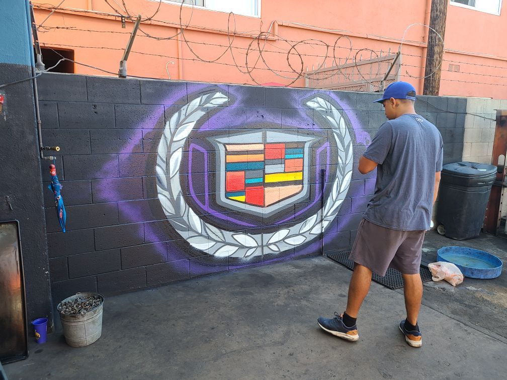 A man is painting a cadillac logo on a wall