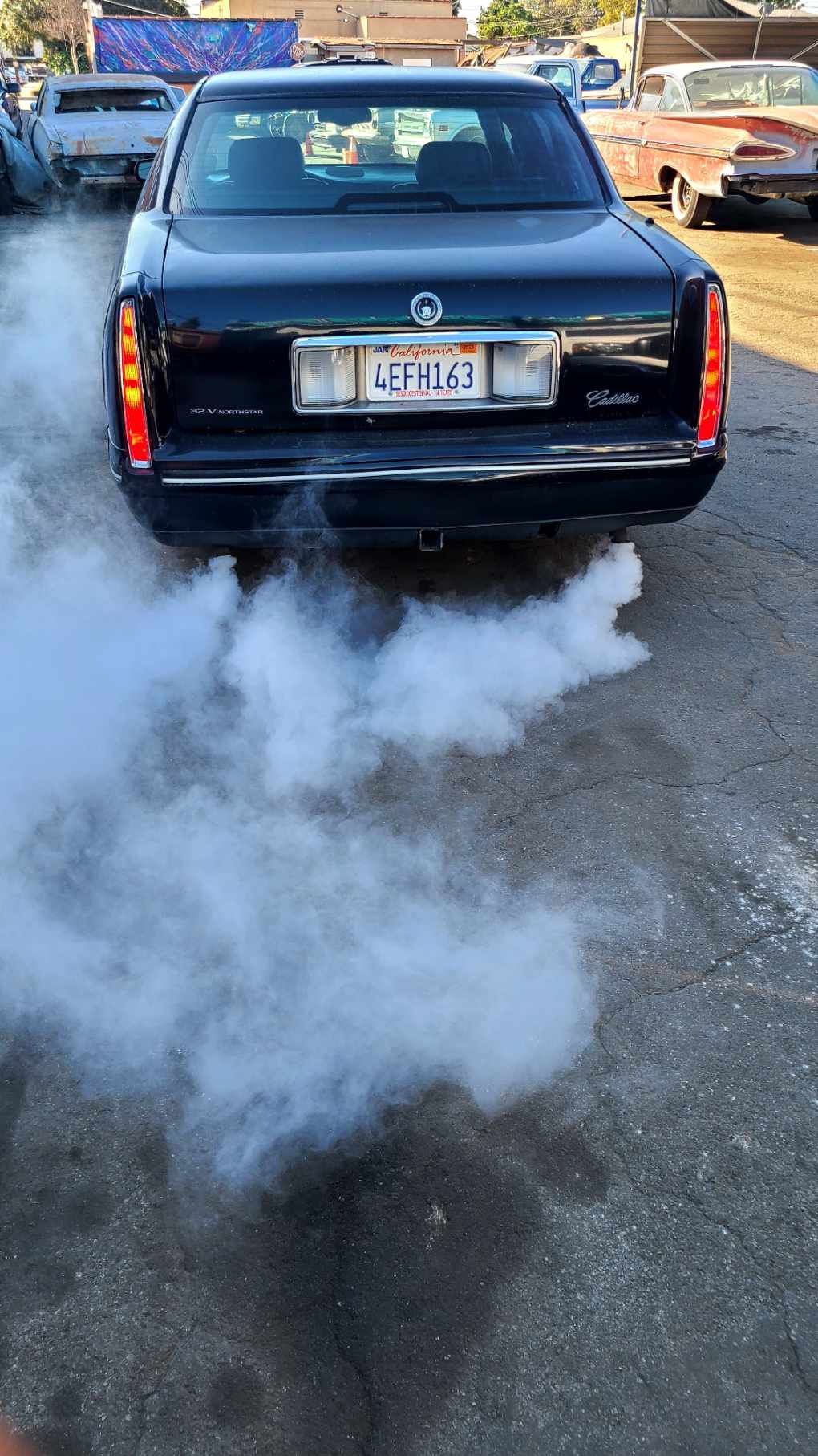 A black car with smoke coming out of its exhaust pipe.