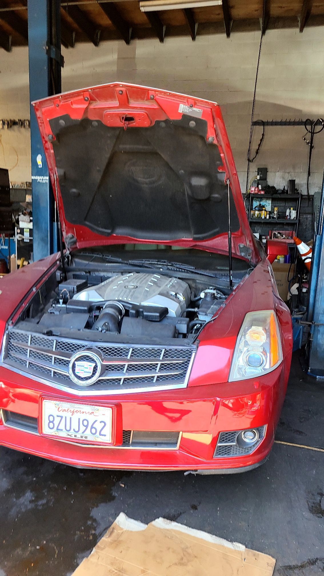A red cadillac with the hood up in a garage