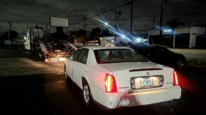 A white car is being towed by a tow truck at night.