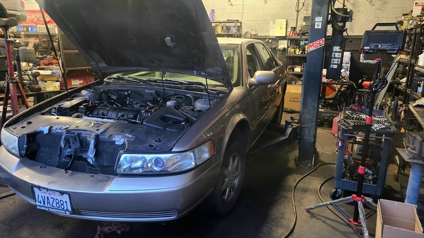 A car with the hood up is sitting on a lift in a garage.
