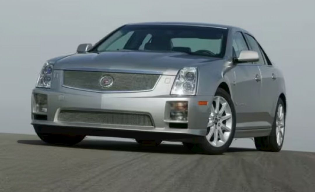 A silver cadillac is driving down a road