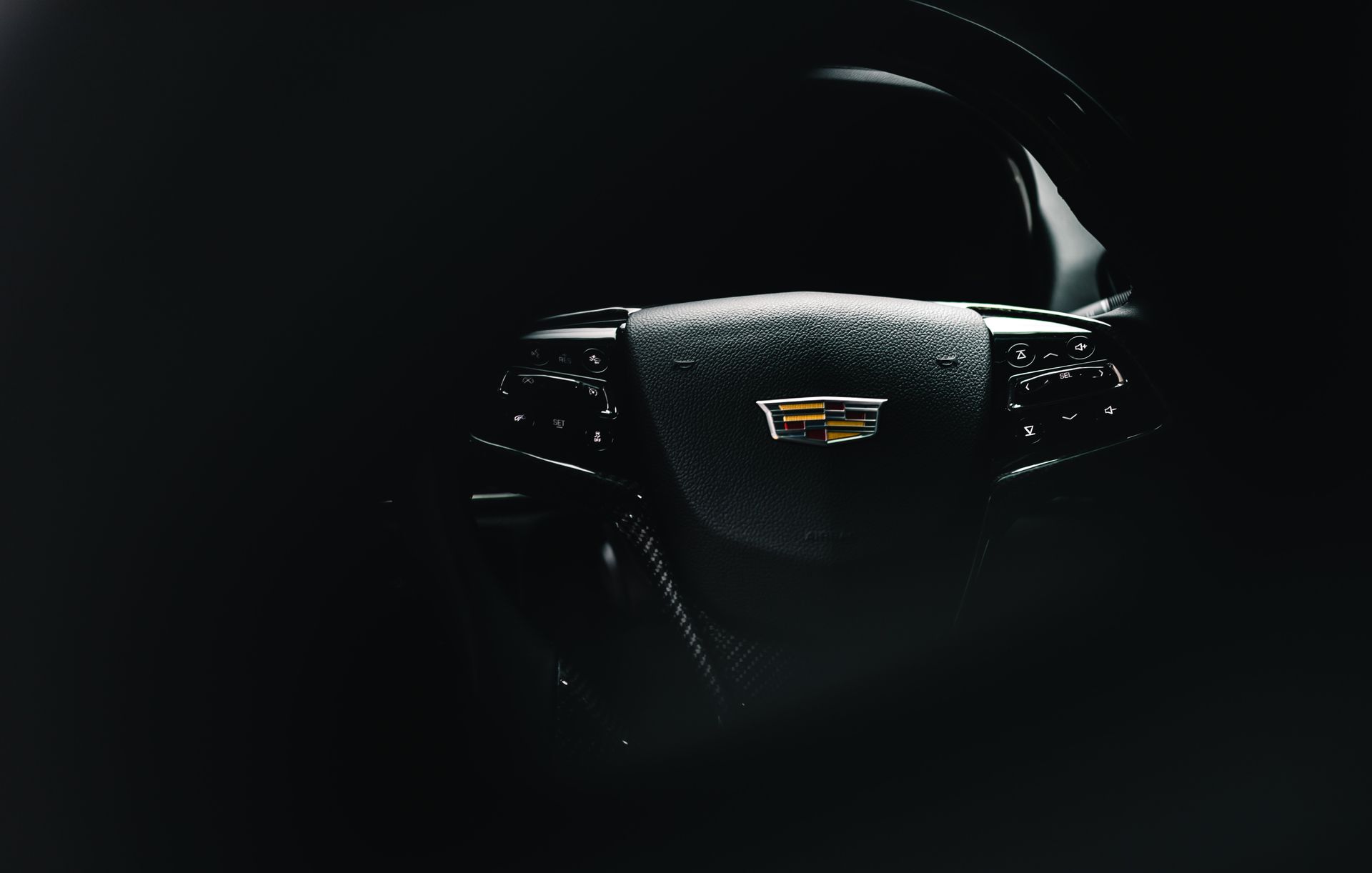 A close up of a cadillac steering wheel in a dark room.