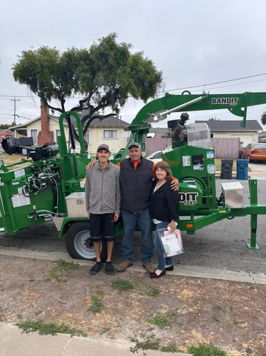 Family posing with a green wood chipper machine outdoors.