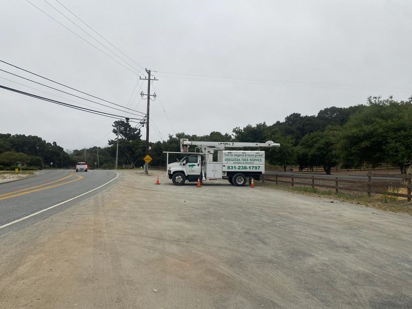 A utility truck parked next to power lines on a rural road. Cloudy sky, trees, and a fence are visible.