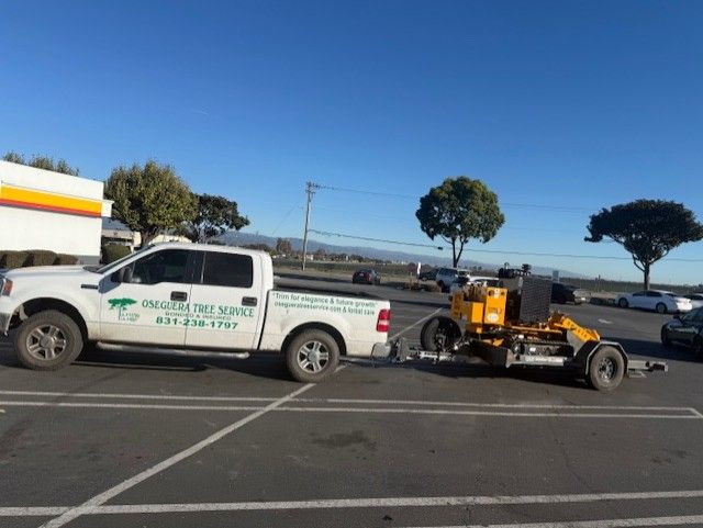 White truck towing a yellow striping machine in a parking lot.