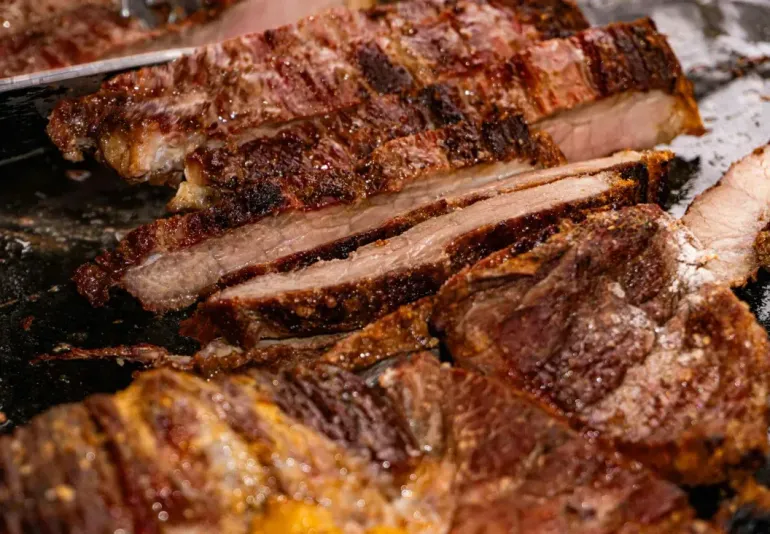Close-up of grilled, charred steak slices with a browned crust on a plate