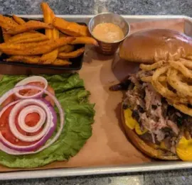 Grilled beef roast sliced to reveal pink center, resting on a wooden board with a fork.