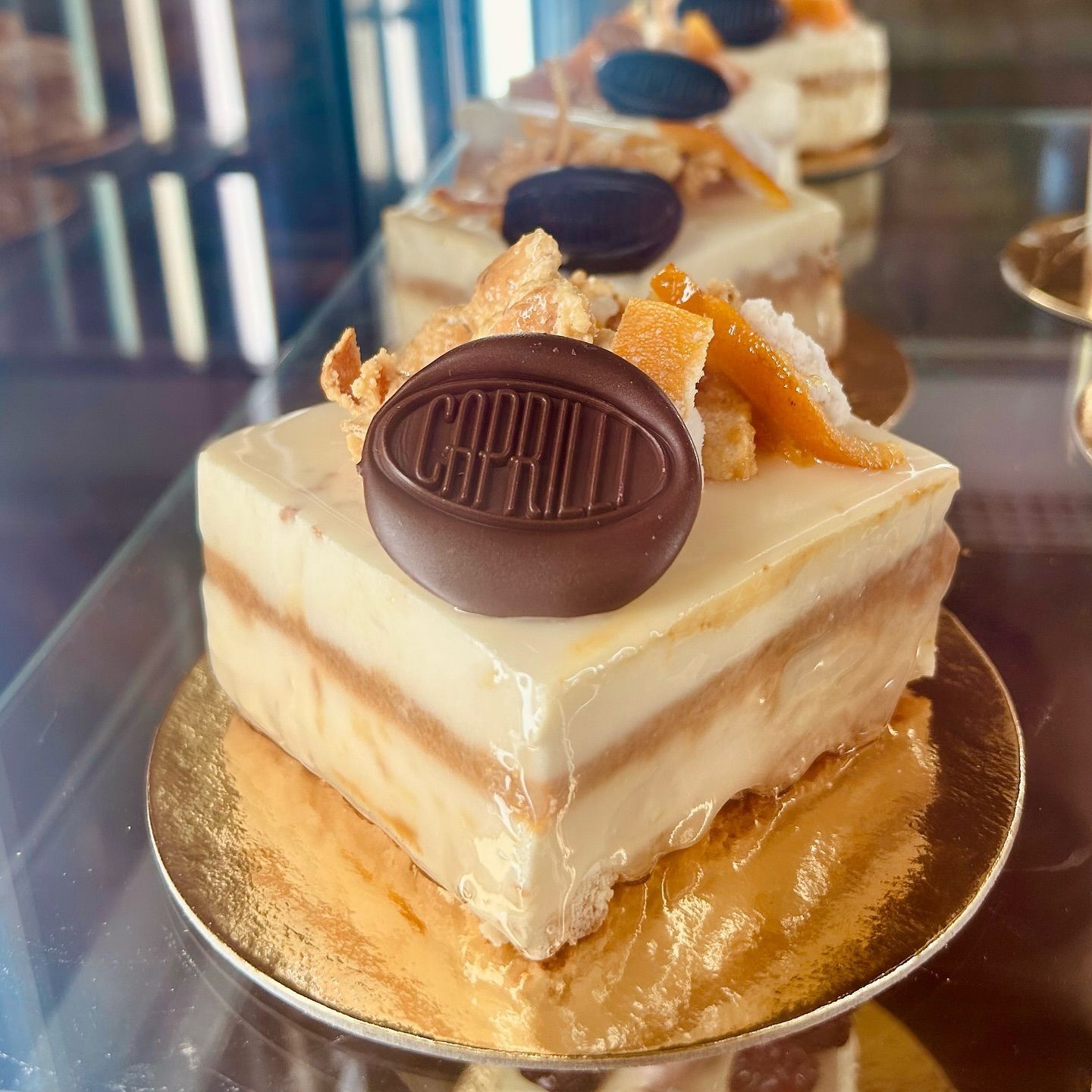 Torta quadrata con medaglione di cioccolato e arancia candita, presentata in una vetrina.