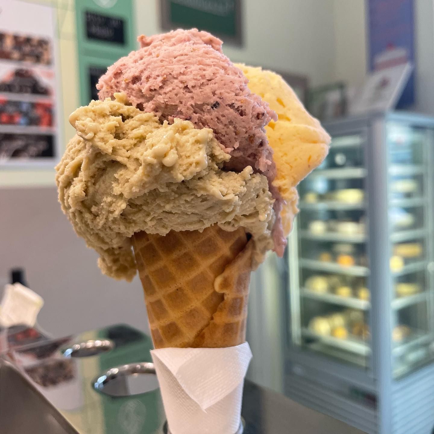Un cono di cialda con tre palline di gelato nelle tonalità del verde, rosa e giallo.