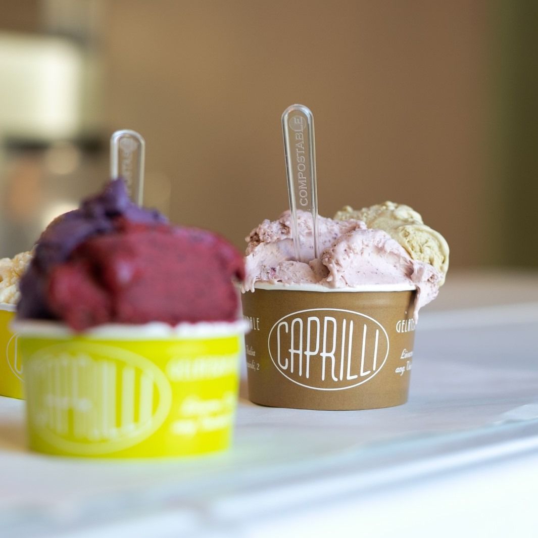 Gelato in coppette di carta con cucchiaini; i gusti disponibili sono viola, rosa e verde.