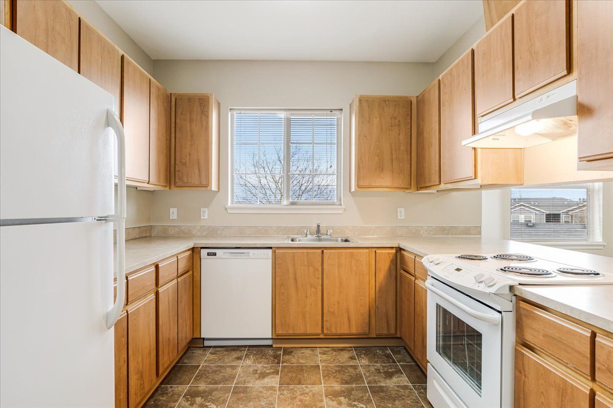 U-shaped kitchen with light wood cabinets, white appliances, and a window above the sink.
