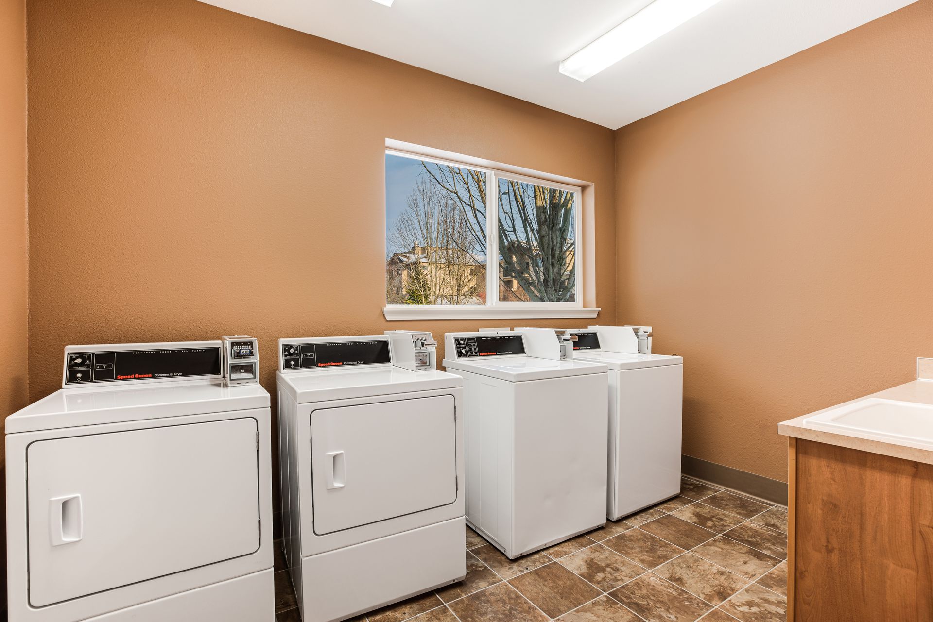 Laundry room with white washers and dryers, brown walls, and a window.