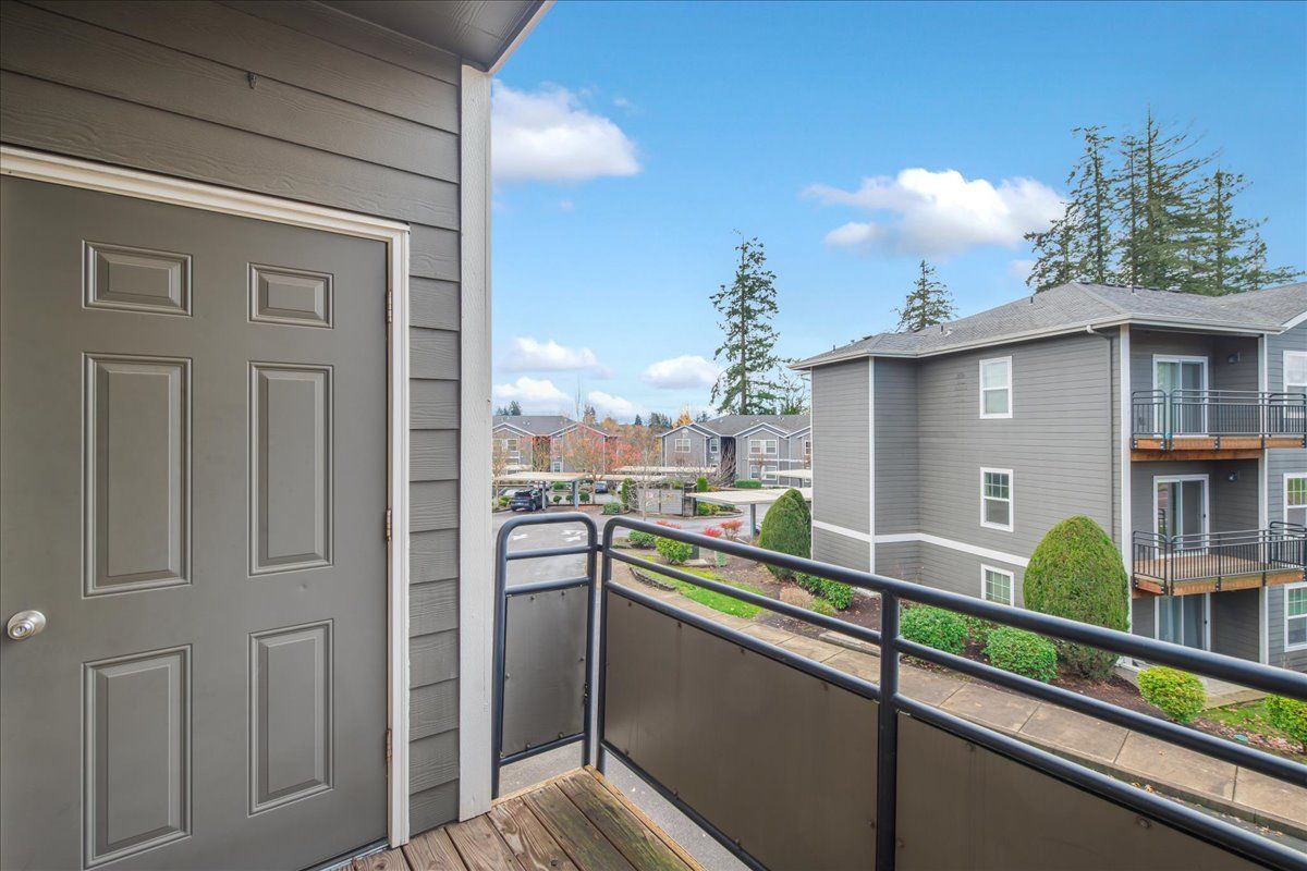 Balcony view of apartment buildings on a sunny day. Gray door, black railing, and blue sky.