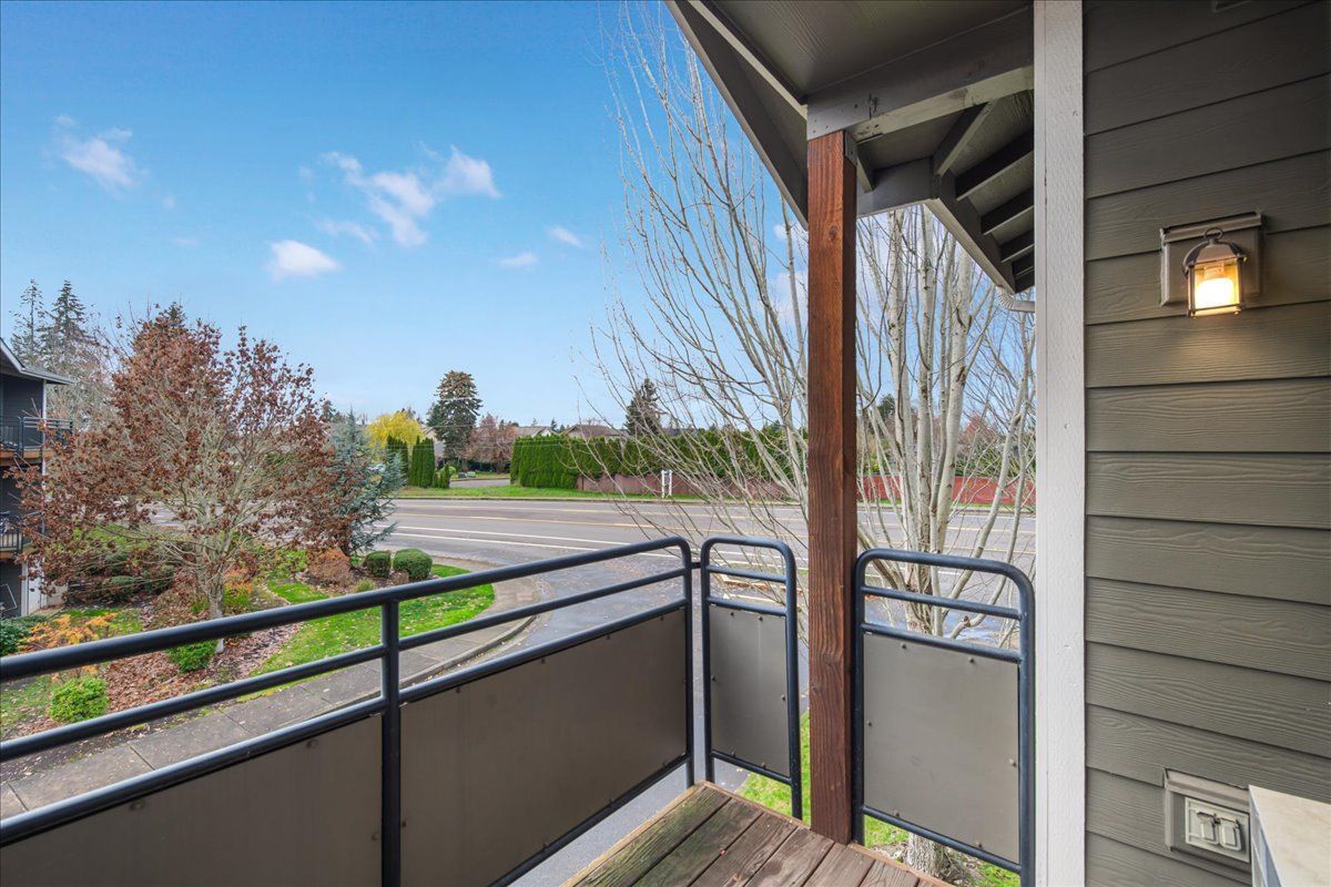 Balcony view of street with railing, green space, gray siding, and a light fixture.