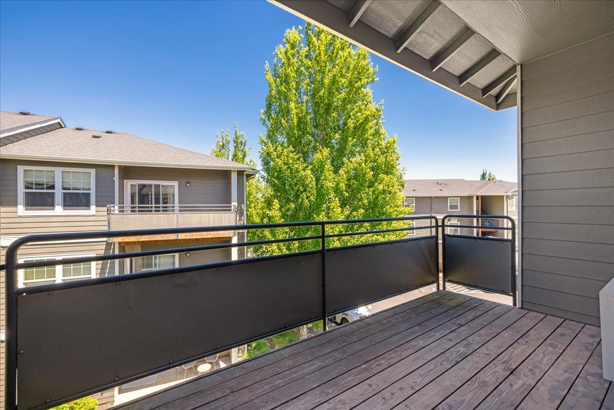 Balcony with gray railing and wooden deck, overlooking apartment buildings and a tree.
