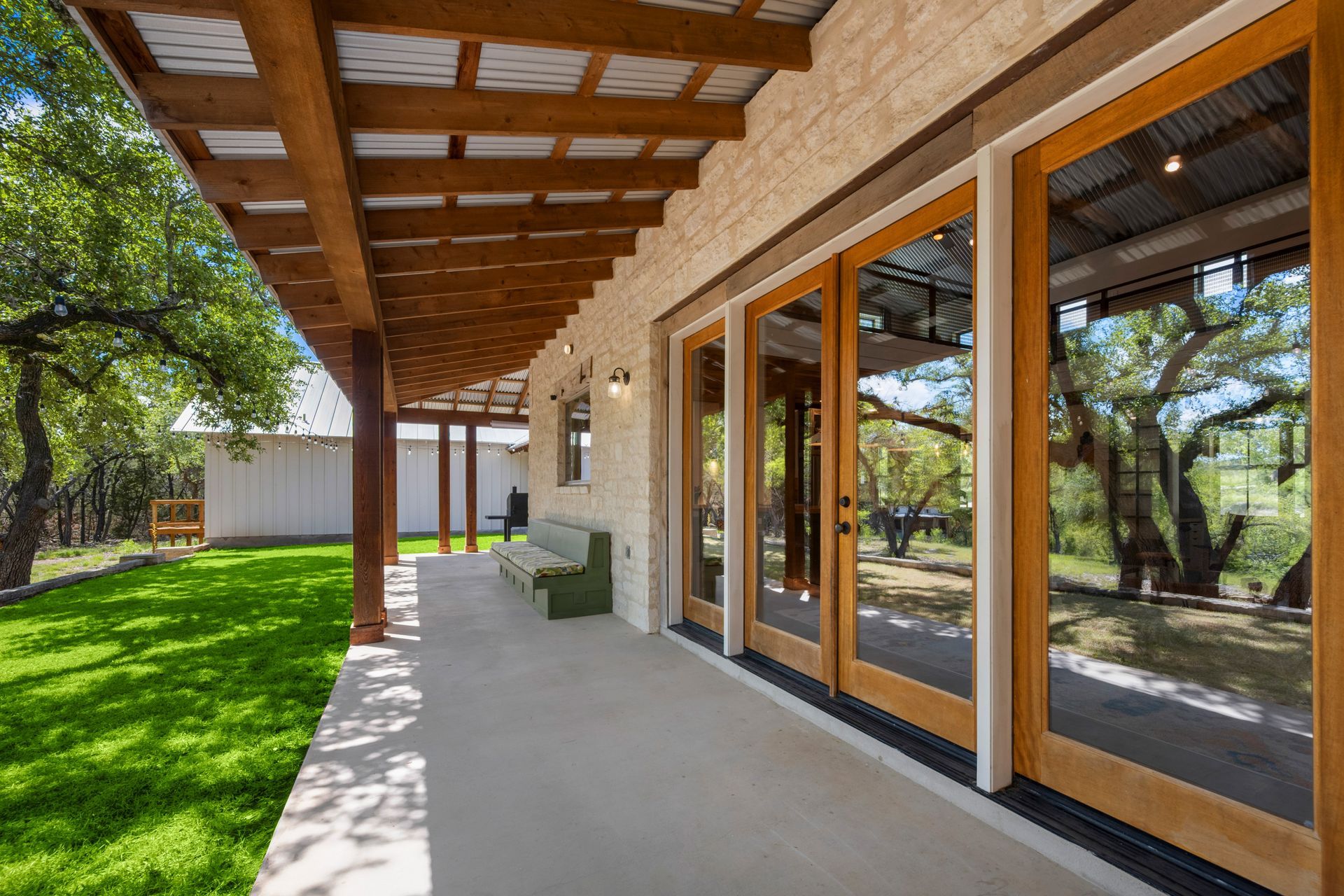 Covered patio with wooden roof, large glass doors, and green lawn beside a modern house