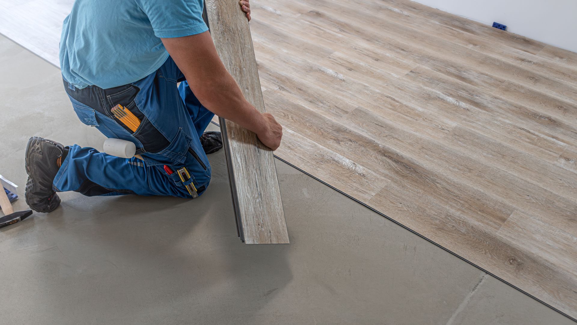 Worker installing wood-look flooring beside a gray concrete floor in a room