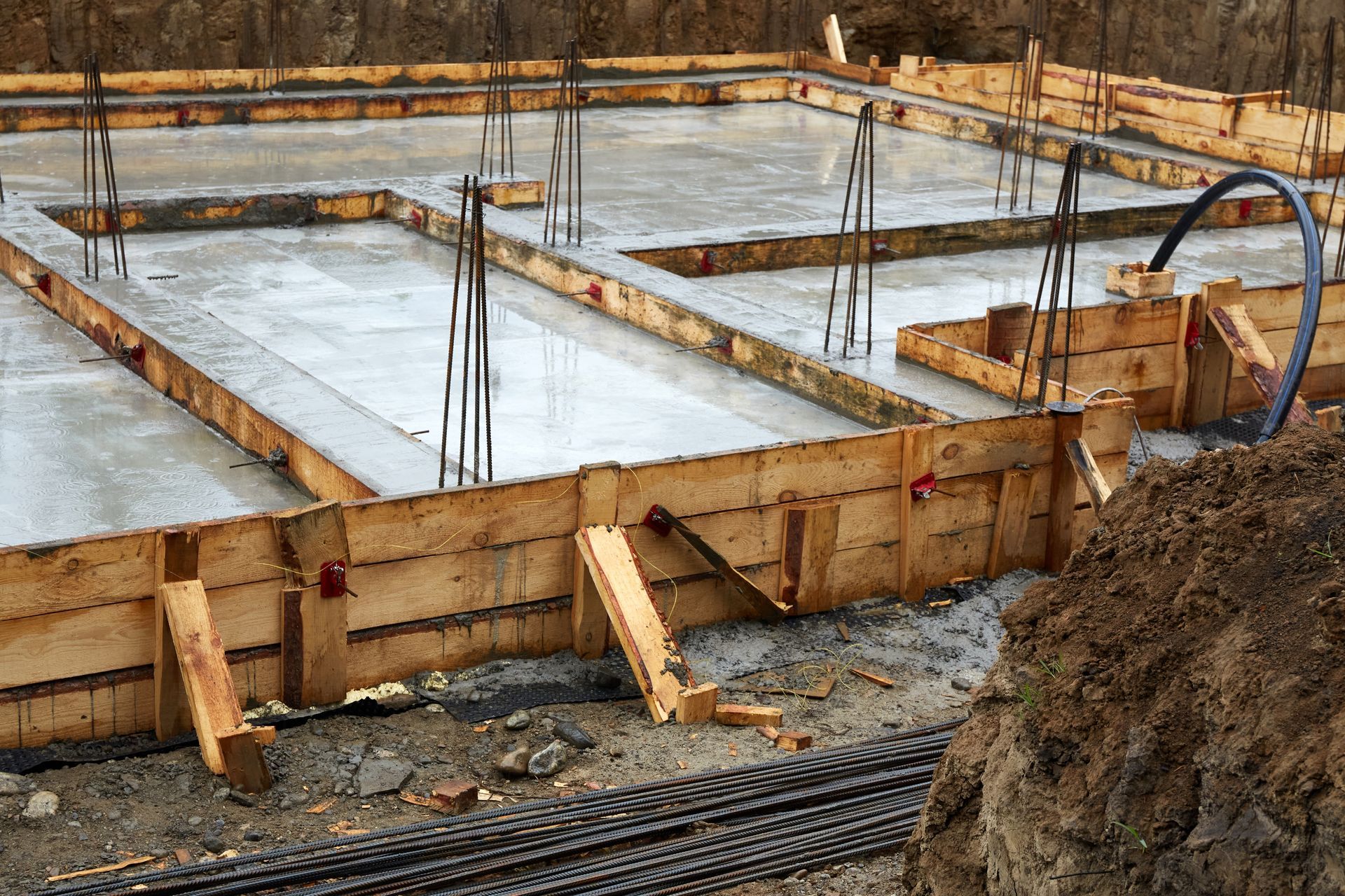 Concrete foundation under construction with wooden forms, rebar, and muddy ground.