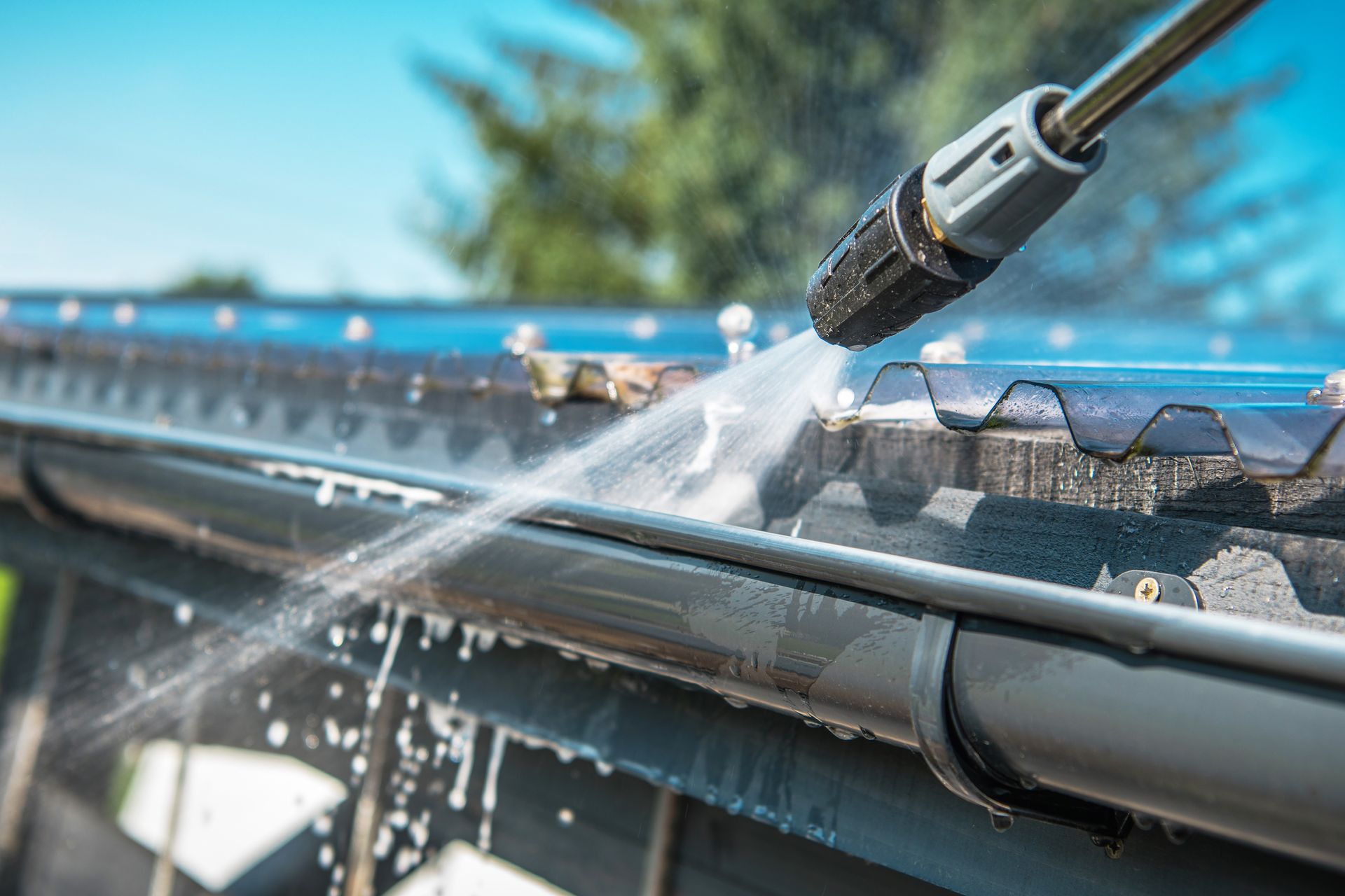 A handyman using a high-pressure water hose to clean gutters and downspouts on a residential building.