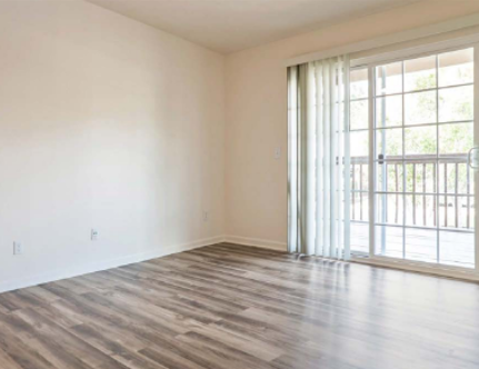 An empty room with white walls, wood-look plank flooring, and a sliding glass door leading to a balcony.