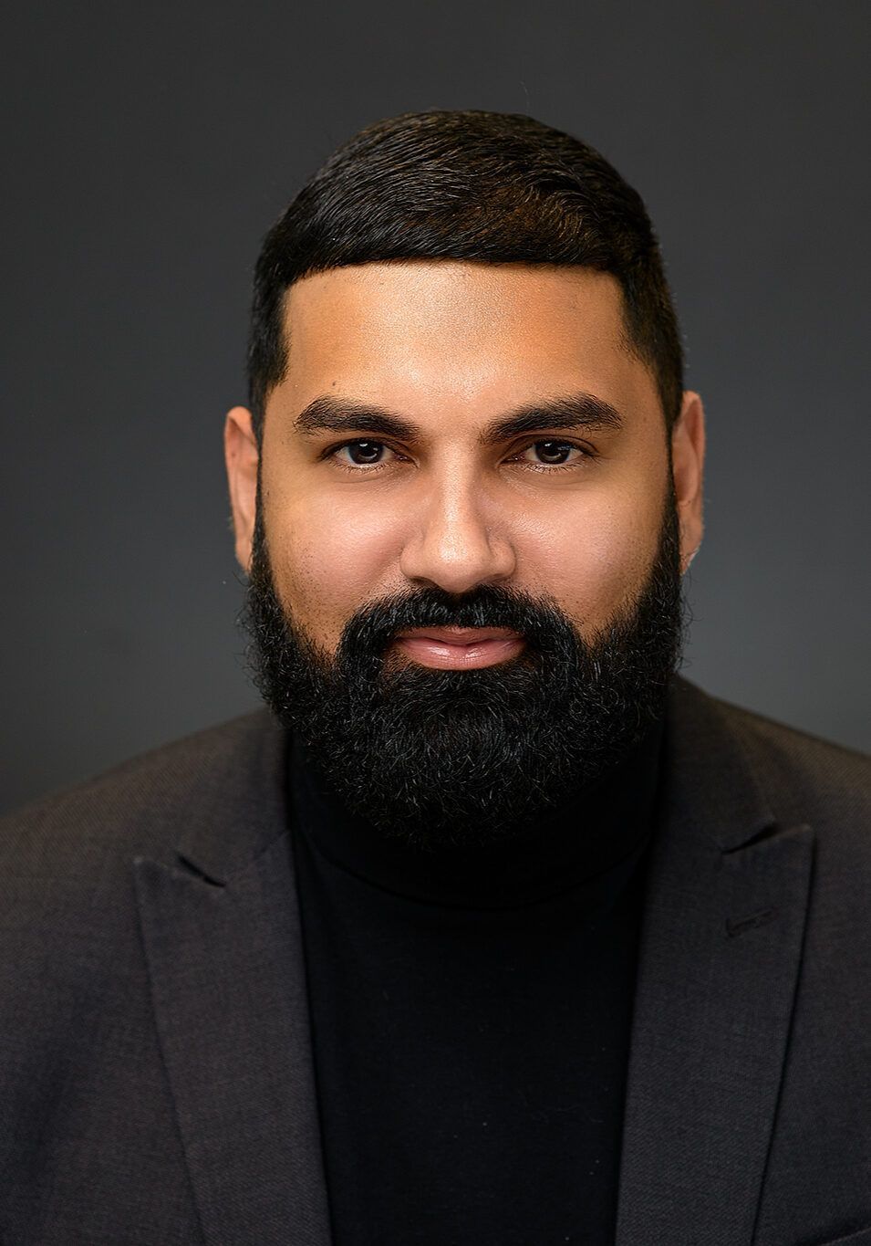 Man with a dark beard and short hair, wearing a black turtleneck and blazer, facing the camera.