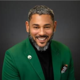 Smiling man in green blazer and black turtleneck; dark background.